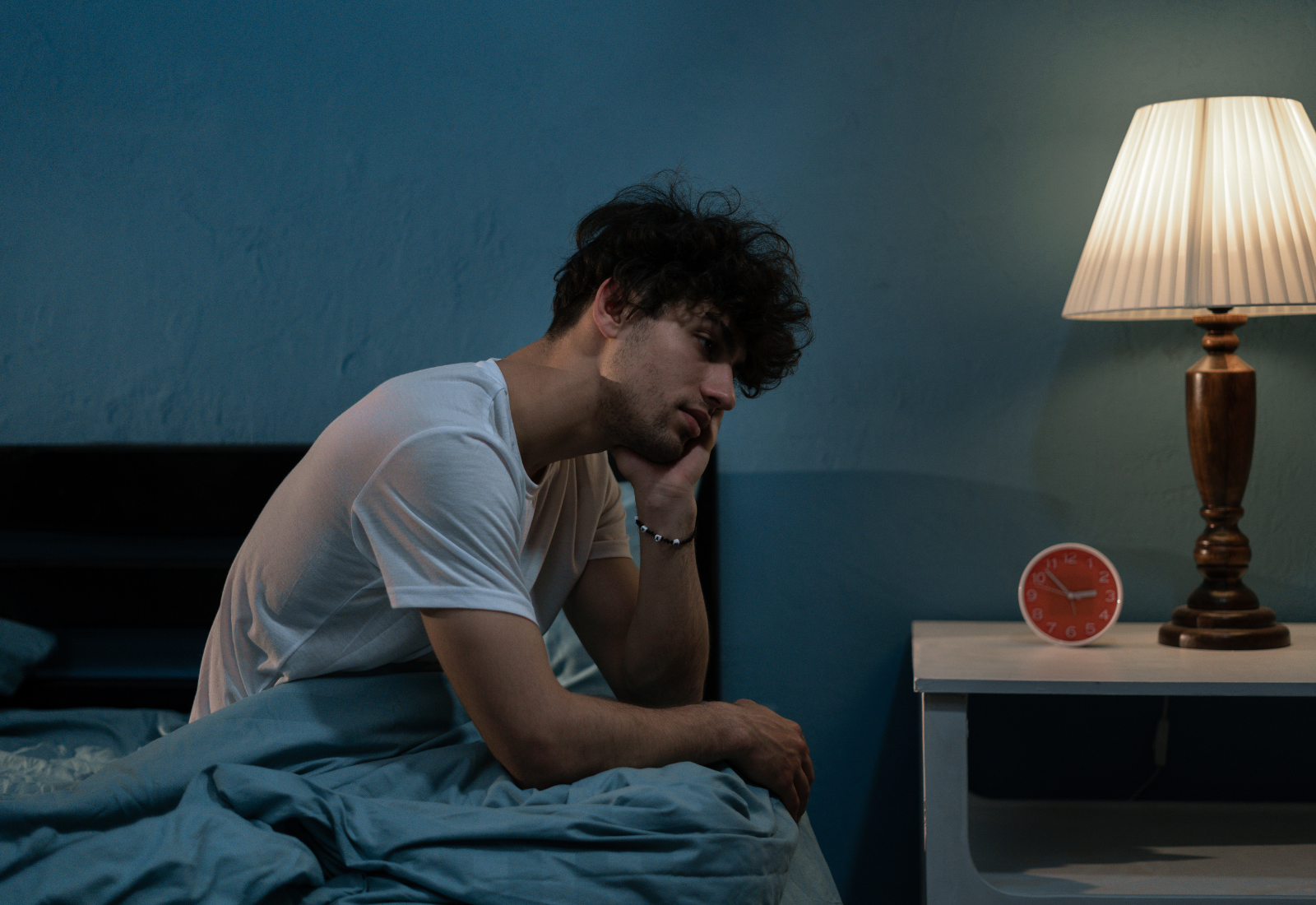 Image of a man appearing depressed sitting on the edge of a bed