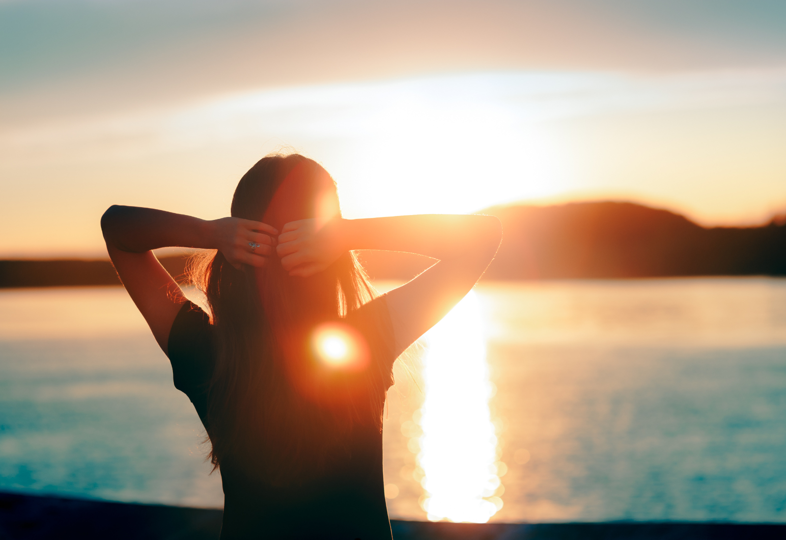 Image of a hopeful woman looking over a body of water at a sunrise